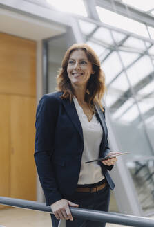 Confident businesswoman holding a tablet in a modern office building - JOSF04146
