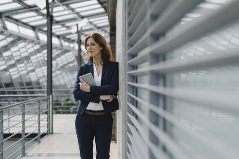 Confident businesswoman holding a tablet in a modern office building - JOSF04152