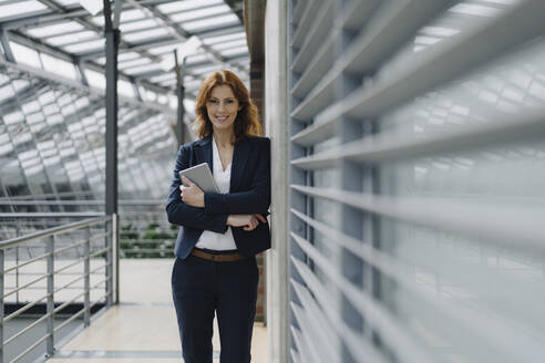 Portrait of a smiling businesswoman holding a tablet in a modern office building - JOSF04153