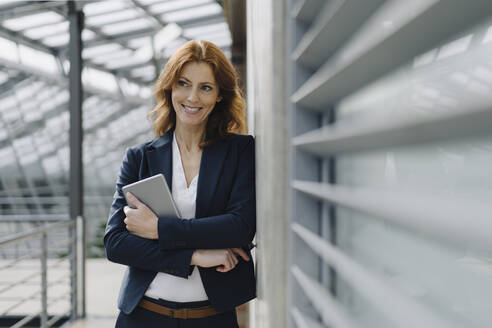Portrait of a smiling businesswoman holding a tablet in a modern office building - JOSF04154