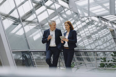 Smiling businessman and businesswoman talking in modern office building - JOSF04158