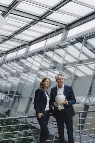 Geschäftsmann und Geschäftsfrau halten Globus in modernem Bürogebäude, lizenzfreies Stockfoto