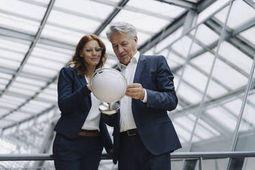 Businessman and businesswoman looking at globe in modern office building - JOSF04163