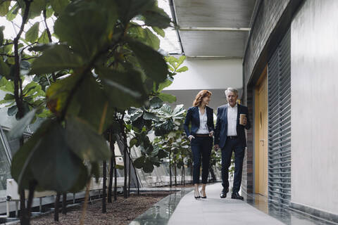 Geschäftsmann und Geschäftsfrau gehen und sprechen in einem modernen Bürogebäude, lizenzfreies Stockfoto