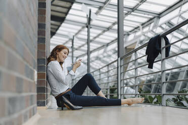 Businesswoman sitting on the floor in office eating muesli - JOSF04190