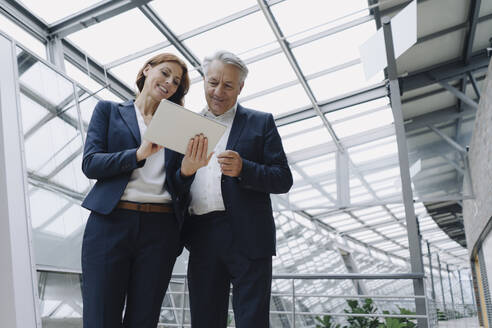 Smiling businessman and businesswoman using tablet in modern office building - JOSF04202