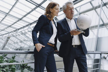 Businessman and businesswoman looking at globe in modern office building - JOSF04203