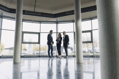 Geschäftsleute im Gespräch am Fenster in einem modernen Bürogebäude, lizenzfreies Stockfoto