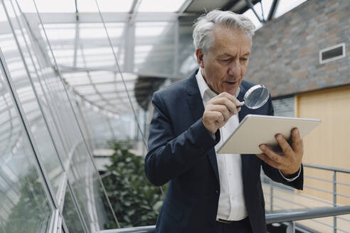 Älterer Geschäftsmann mit Vergrößerungsglas, der im Büro ein Tablet liest - JOSF04219