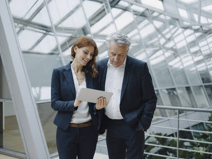 Smiling businessman and businesswoman using tablet in modern office building - JOSF04223