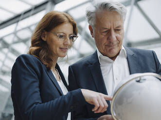 Businessman and businesswoman looking at globe in office - JOSF04226