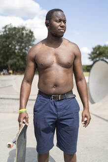 Junger Mann, der im Skatepark steht und ein Skateboard hält - FBAF01123