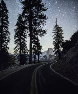 Straße vorbei an Silhouettenbäumen im Yosemite National Park gegen den Sternenhimmel bei Nacht - CAVF72518