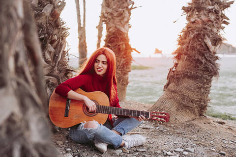 Porträt einer jungen Frau, die am Strand Gitarre spielt, Almunecar, Spanien, lizenzfreies Stockfoto