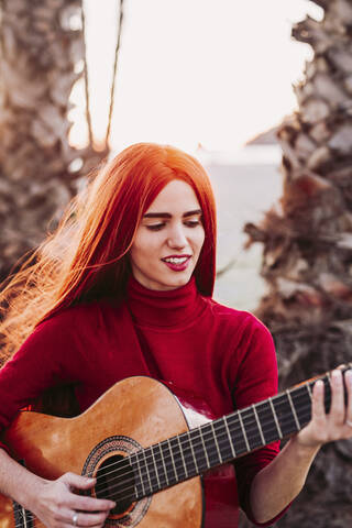 Porträt einer rothaarigen jungen Frau, die am Strand Gitarre spielt, Almunecar, Spanien, lizenzfreies Stockfoto