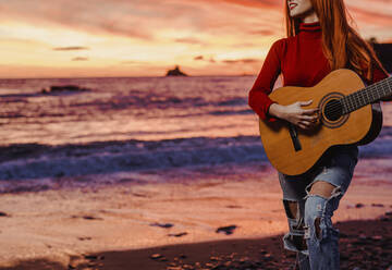 Crop view of young woman playing guitar on the beach at sunset, Almunecar, Spain - LJF01221