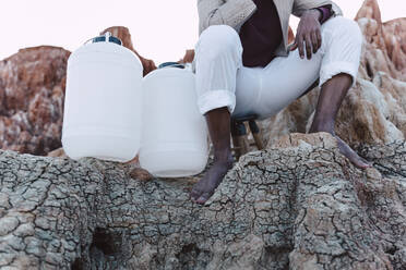 Mann mit leeren Wasserkanistern auf einem Felsen sitzend - ERRF02431