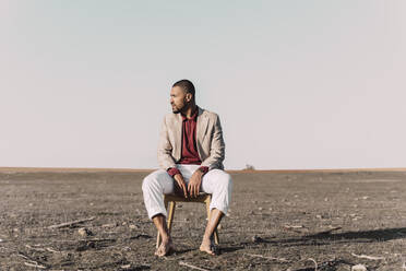 Young man sitting on chair in barren land - ERRF02443