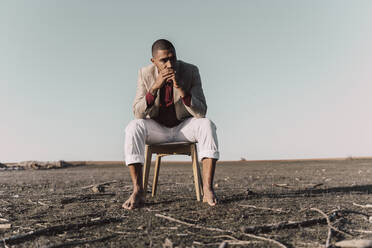 Young man sitting on chair in barren land - ERRF02446