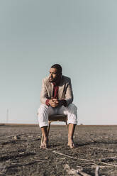 Young man sitting on chair in barren land - ERRF02448