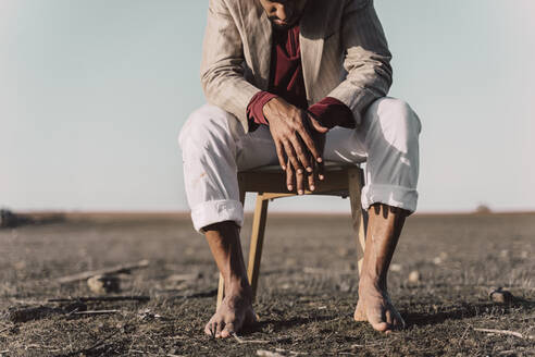 Low section of young man sitting on chair in barren land - ERRF02450