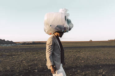 Junger Mann trägt eine Tasche mit Plastikflaschen auf dem Kopf in einem kargen Land - ERRF02485
