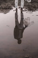 Tiefschnitt eines Mannes mit Plastikflaschen, der an einem Wasserloch steht - ERRF02503