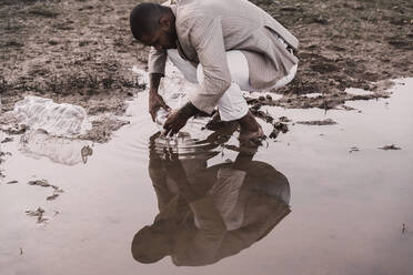 Junger Mann füllt Plastikflasche mit Wasser an einem Wasserloch - ERRF02504