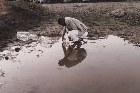Junger Mann füllt Plastikflasche mit Wasser an einem Wasserloch - ERRF02505