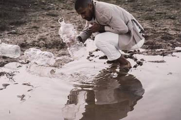 Junger Mann füllt Plastikflasche mit Wasser an einem Wasserloch - ERRF02506