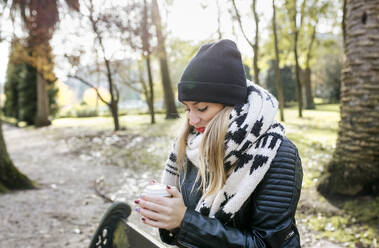 Beautiful blond woman having a take away coffee in a park - MGOF04231