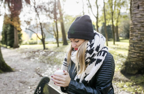 Schöne blonde Frau mit einem Kaffee zum Mitnehmen in einem Park - MGOF04231
