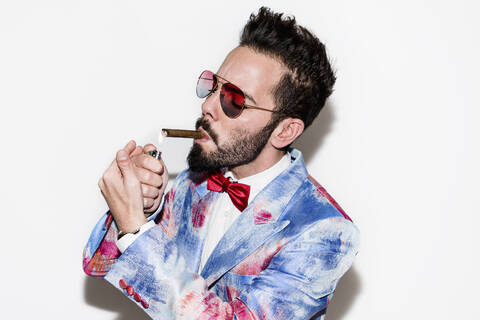 Cool and stylish man wearing a colorful suit and sunglasses lighting a cigar stock photo