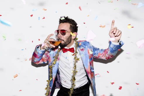 Cool and stylish man wearing a colorful suit and sunglasses celebrating a party with confetti and drinking - LOTF00087