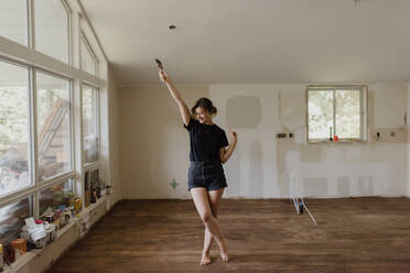 Woman holding paintbrush and dancing in new home - CUF54379