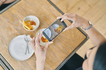 Woman taking photograph of food in restaurant - CUF54410