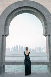 Rückenansicht einer Frau, die das Meer und die Wolkenkratzer von Doha beobachtet - CAVF72571