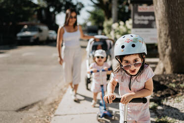 Mother and daughters playing push scooter in neighbourhood - ISF23509