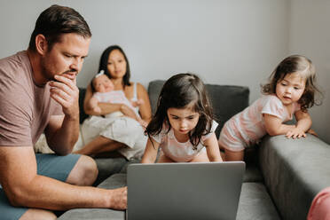 Fünfköpfige Familie, die sich auf der Couch im Wohnzimmer entspannt und einen Laptop benutzt - ISF23514