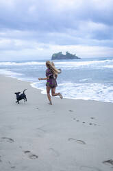 Frau läuft mit Hund am Strand nach Sonnenuntergang, Cahuita, Costa Rica - ISF23526