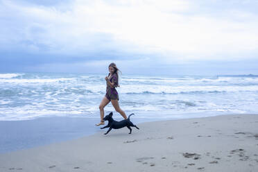 Frau läuft mit Hund am Strand nach Sonnenuntergang, Cahuita, Costa Rica - ISF23529