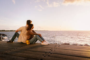 Paar sitzt Rücken an Rücken auf dem Sitz und schaut bei Sonnenuntergang aufs Meer - MASF16007