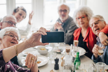 Frau, die im Restaurant sitzend mit ihrem Smartphone ein Foto von ihren älteren Freunden macht - MASF16040