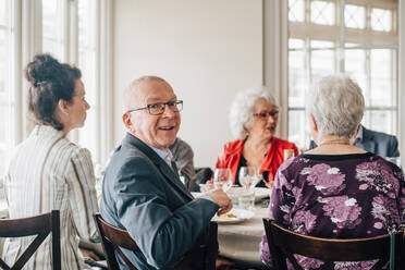 Porträt eines älteren Mannes, der lächelnd bei Freunden im Restaurant sitzt - MASF16043