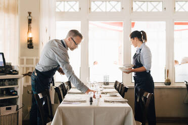 Männliche und weibliche Mitarbeiter arrangieren einen Tisch im Restaurant - MASF16054