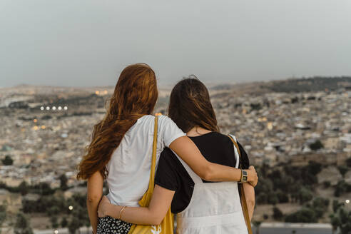 Back view of two best friends enjoying city view arm in arm in the evening, Fez, Morocco - AFVF04811