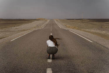 Back view of woman crouching on median strip of empty country road, Fez, Morocco - AFVF04823