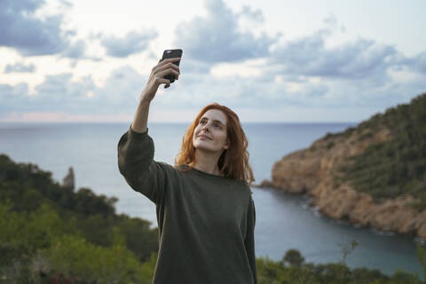 Rothaarige junge Frau macht ein Selfie an der Küste, Ibiza, Spanien, lizenzfreies Stockfoto