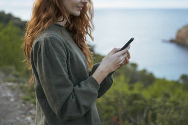 Redheaded young woman using cell phone at the coast, Ibiza, Spain - AFVF04838