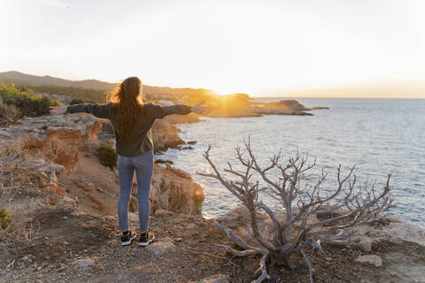 Redheaded young woman standing at the coast at sunset, Ibiza, Spain stock photo